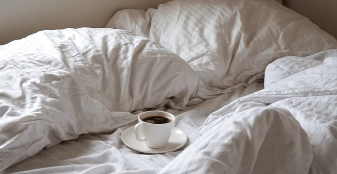 Una taza de café se sienta en un plato en una cama con las mantas echadas hacia atrás